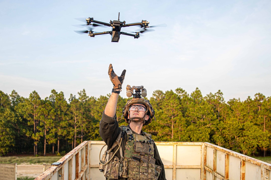 A solider reaches up to a drone while standing outside in unifom.