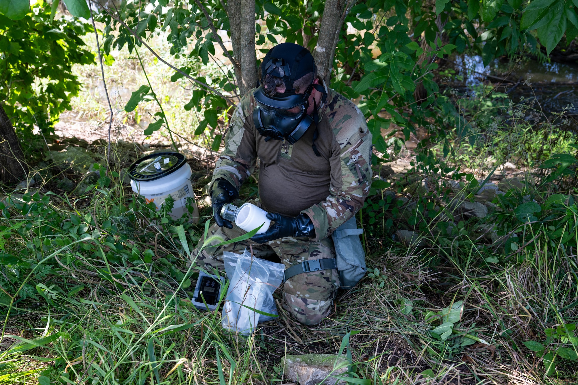 A man in a gas mask collects samples into a bottle