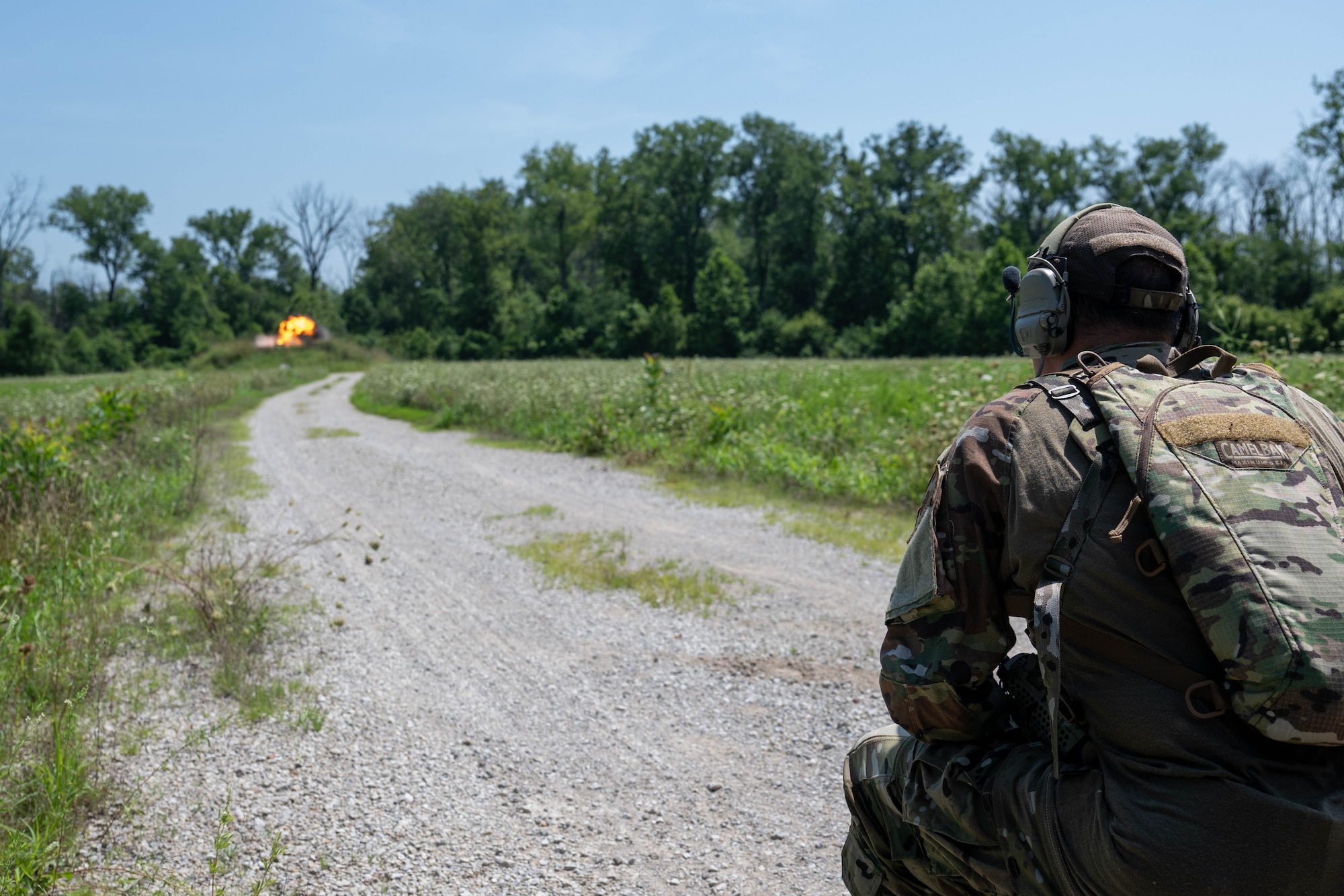 A man crouches down while he watches an explosion in the distance