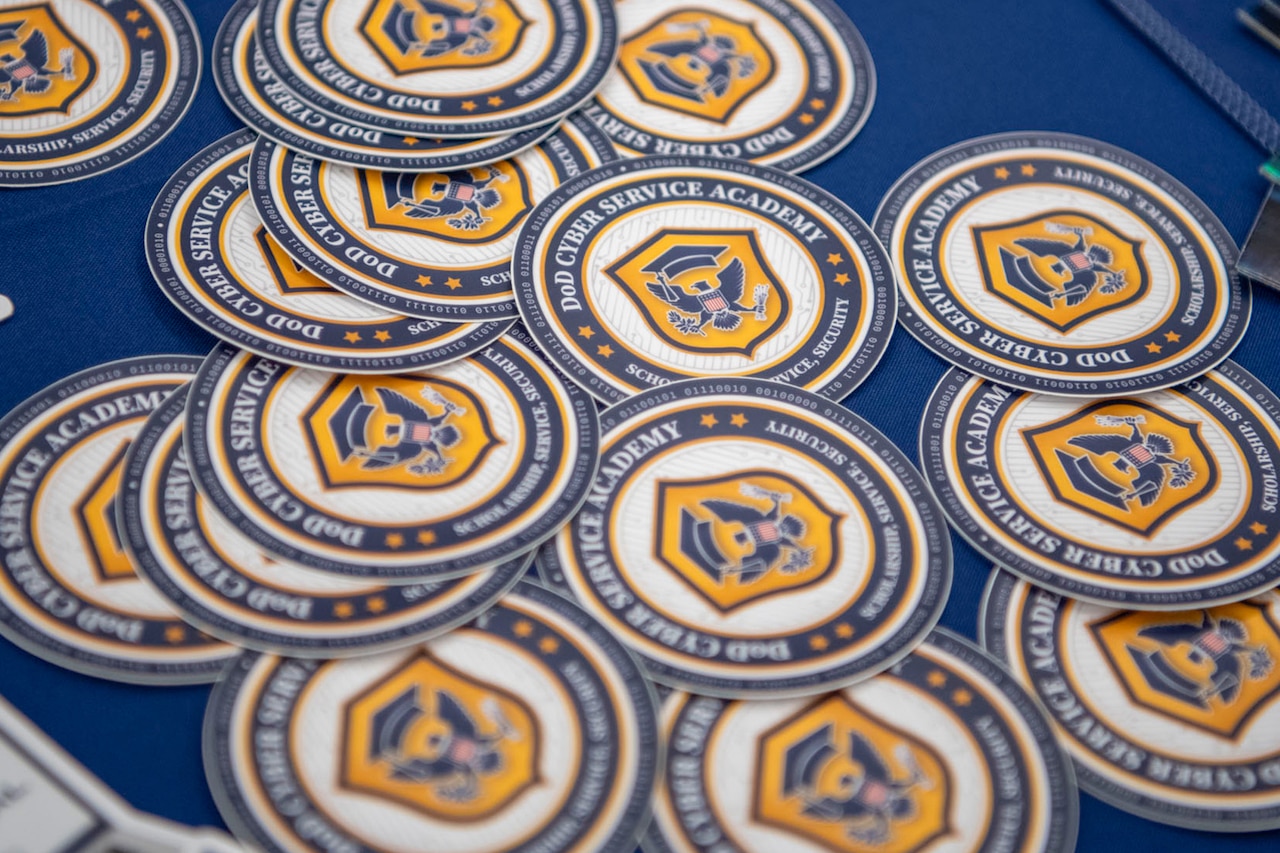 A collection of round blue and yellow stickers with a logo sits on a table covered in a blue tablecloth.