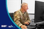 Uniformed service member uses mouse and keyboard, looking at desktop screen.