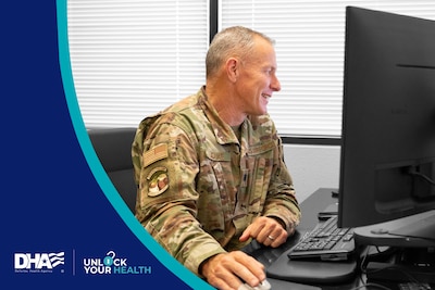 Uniformed service member uses mouse and keyboard, looking at desktop screen.