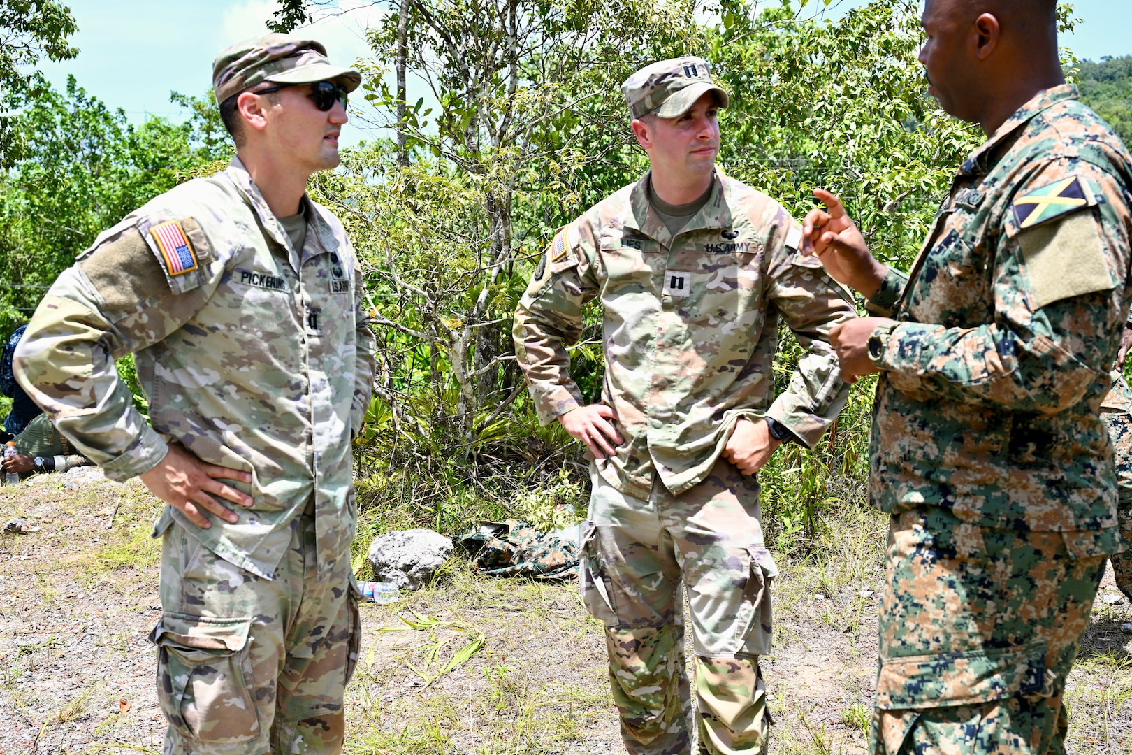 U.S. Army Capt. Chad Pickering, incoming Bilateral Affairs Officer (BAO), and U.S. Capt. Aaron Lies, outgoing BAO, speak with a Jamaica Defense Force (JDF) soldier at Moneague Training Camp, St. Ann, during the Caribbean Regional Training Camp 2025, held July 12-27 across Jamaica. The District of Columbia National Guard's (DCNG) partnership with Jamaica, facilitated by the U.S. National Guard Bureau's State Partnership Program, promotes security cooperation through military engagements and interagency collaboration.