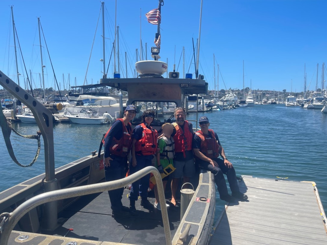 Two Coast Guardsmen and an Auxiliarist are seen posing for a picture with a child and their father aboard a 26-foot Trailerable-Aids-to-Navigation Boat.