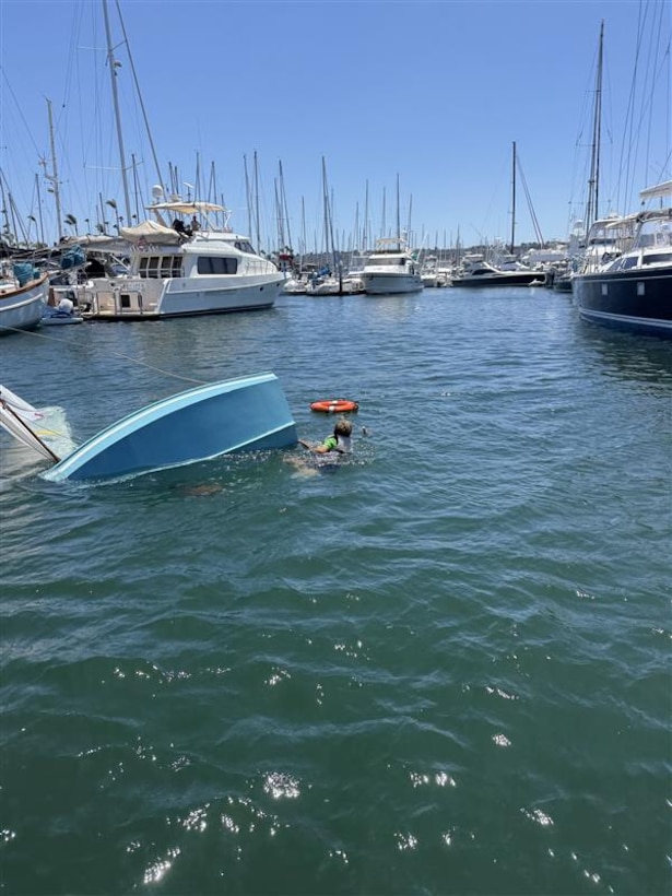A child is seen in the water next to a capsized sailing vessel.