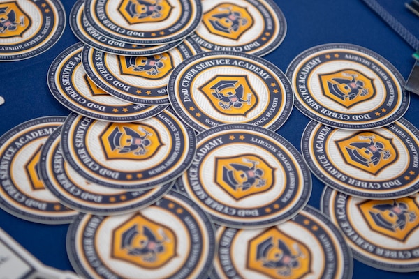 A collection of round blue and yellow stickers with a logo sits on a table covered in a blue tablecloth.