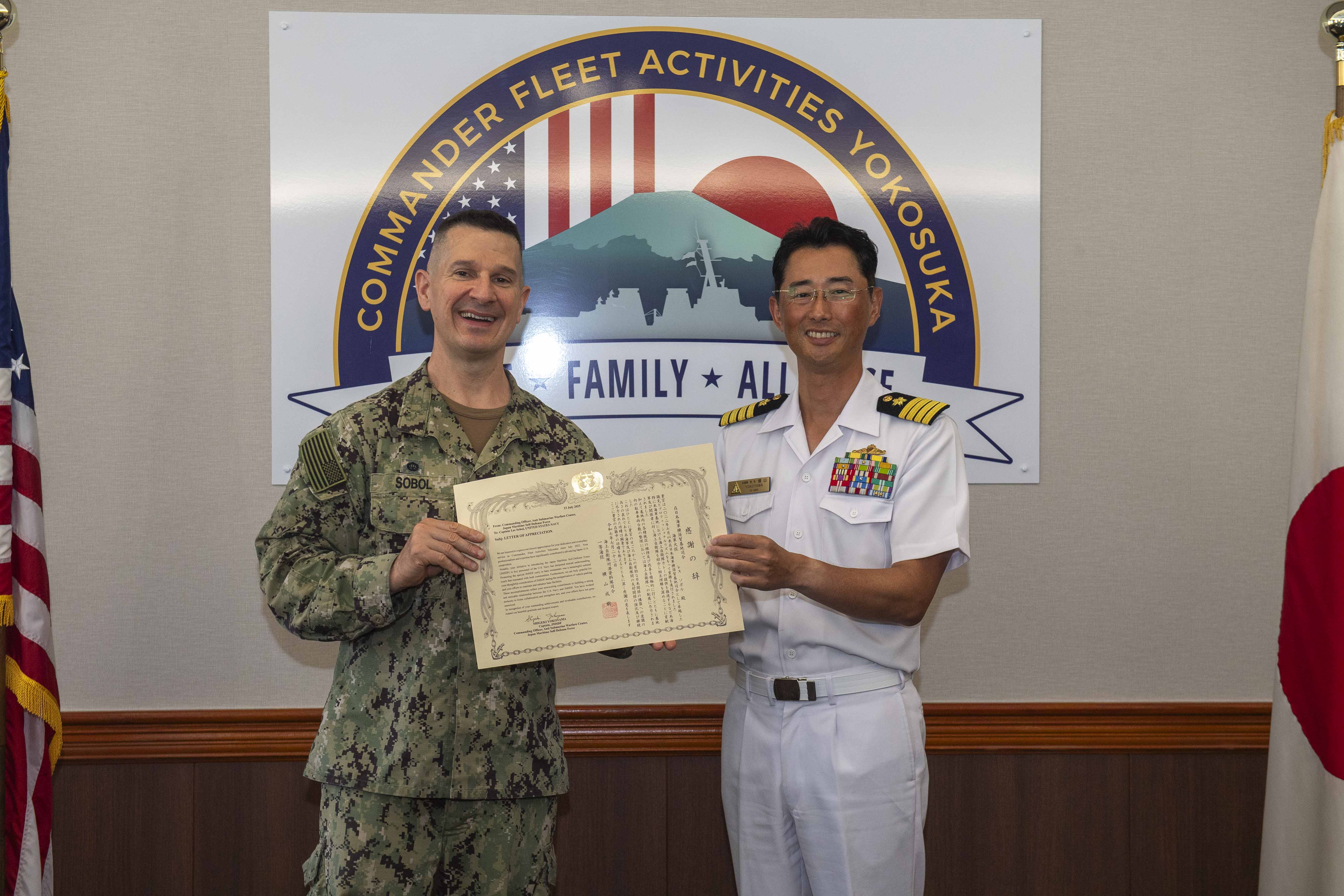 Capt. Les Sobol, Commander, Fleet Activities Yokosuka (CFAY), left, receives a Letter of Appreciation from Japan Maritime Self-Defense Force Capt. Shigeki Yokoyama, commanding officer, Anti-Submarine Warfare Center, during an office visit at CFAY headquarters July 23, 2025.