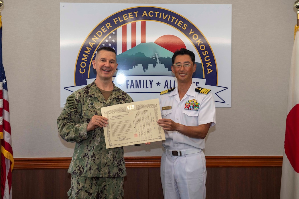 Capt. Les Sobol, Commander, Fleet Activities Yokosuka (CFAY), left, receives a Letter of Appreciation from Japan Maritime Self-Defense Force Capt. Shigeki Yokoyama, commanding officer, Anti-Submarine Warfare Center, during an office visit at CFAY headquarters July 23, 2025.