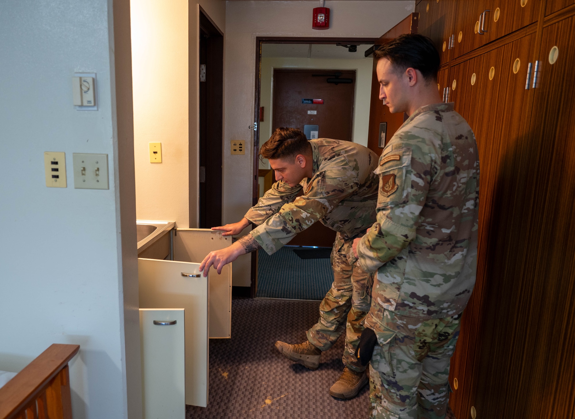 Two service members inspect cabinet.