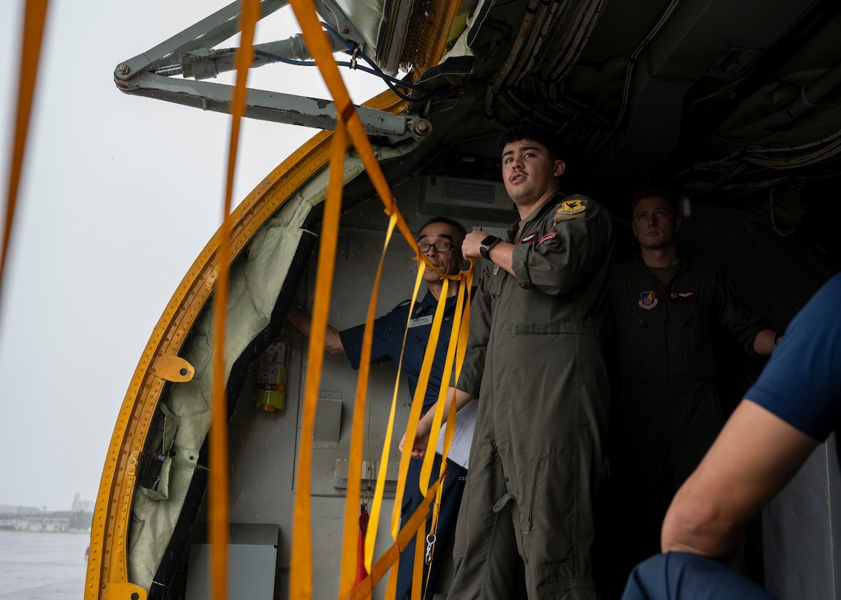 A military member unhooks yellow straps from the inside of an aircraft.