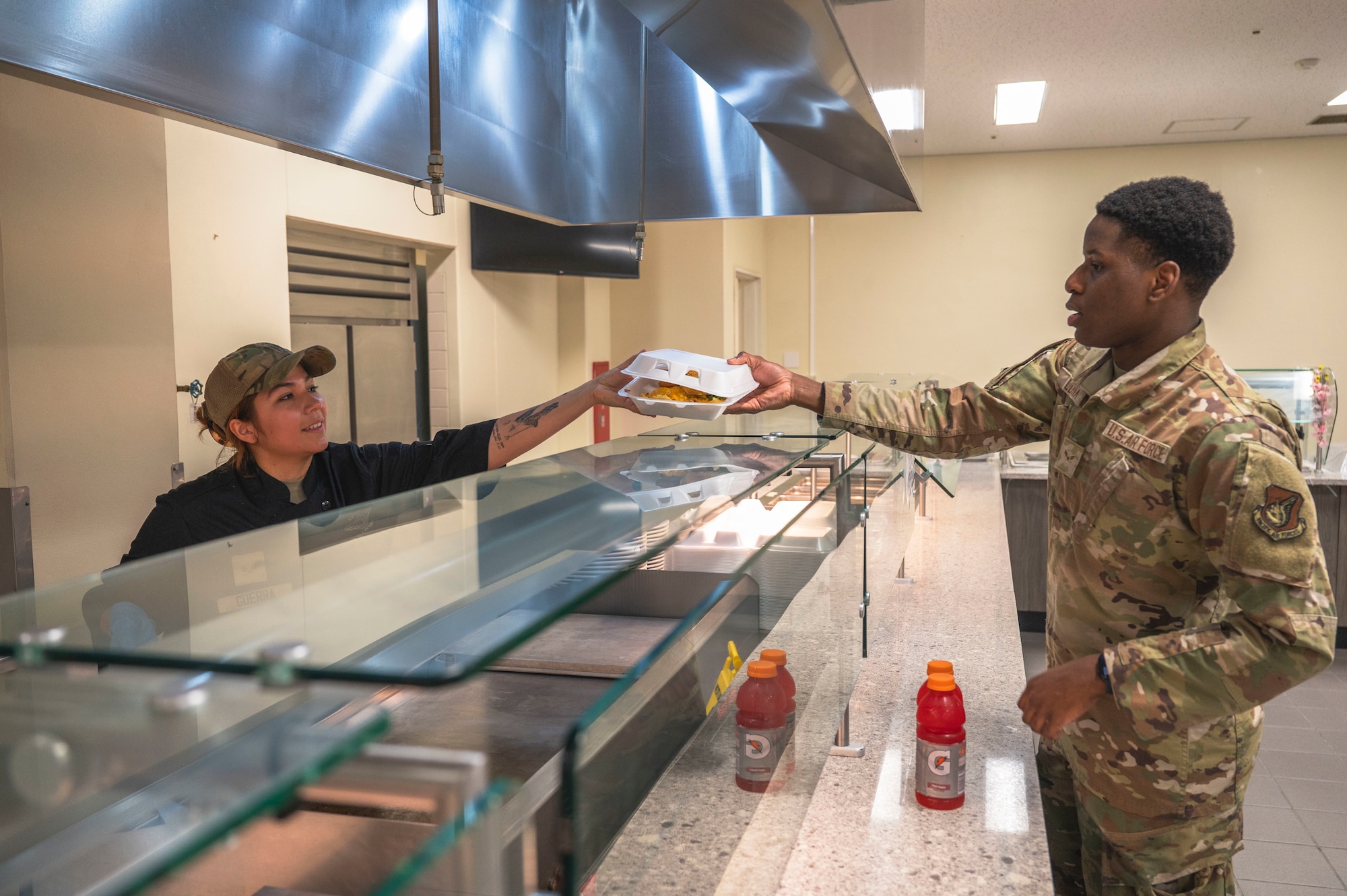 U.S. Air Force Senior Airman Nikko Guerra, left, 18th Force Support Squadron food services shift lead, hands food to Airman 1st Class Gavin Lunn, 18th Logistics Readiness Squadron supply journeyman during the midnight service at the Marshall Dining Facility on Kadena Air Base, Japan, July 24, 2025.