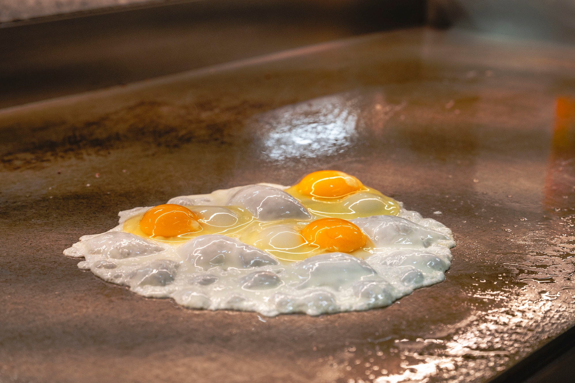 Three eggs sizzle on a stovetop at the Marshall Dining Facility on Kadena Air Base, Japan, July 24, 2025.