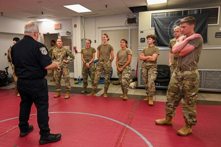 U.S. Air Force Academy cadets gather around Sgt. 1st Class Lance LaRue, a police trainer with the 11th Security Forces Squadron, as he instructs taser exposure training during a USAFA Summer Operations visit at Joint Base Anacostia-Bolling, Washington, D.C., July 16, 2025. Several of the cadets voluntarily experienced the effects of taser deployment during the training, which is a mandatory certification for all Security Forces members. (U.S. Air Force photo by Airman 1st Class Shanel Toussaint)