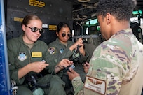 U.S. Air Force Senior Airman Rashad Nunez, right, a special missions aviator with the 1st Helicopter Squadron, assists U.S. Air Force Academy Cadets Caitlyn Budd, left, and Keerthanaa Narasingu don headsets at Joint Base Andrews, Md., July 17, 2025. Cadets visited JBA and Joint Base Anacostia-Bolling, Washington, D.C., as part of USAFA’s Summer Operations program to learn more about officer life and the operational Air Force. (U.S. Air Force photo by Hayden Hallman)