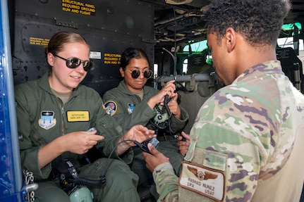 U.S. Air Force Senior Airman Rashad Nunez, right, a special missions aviator with the 1st Helicopter Squadron, assists U.S. Air Force Academy Cadets Caitlyn Budd, left, and Keerthanaa Narasingu don headsets at Joint Base Andrews, Md., July 17, 2025. Cadets visited JBA and Joint Base Anacostia-Bolling, Washington, D.C., as part of USAFA’s Summer Operations program to learn more about officer life and the operational Air Force. (U.S. Air Force photo by Hayden Hallman)
