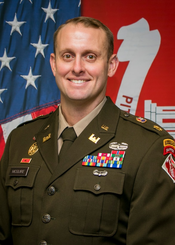 A man in military uniform standing in front of a flag.