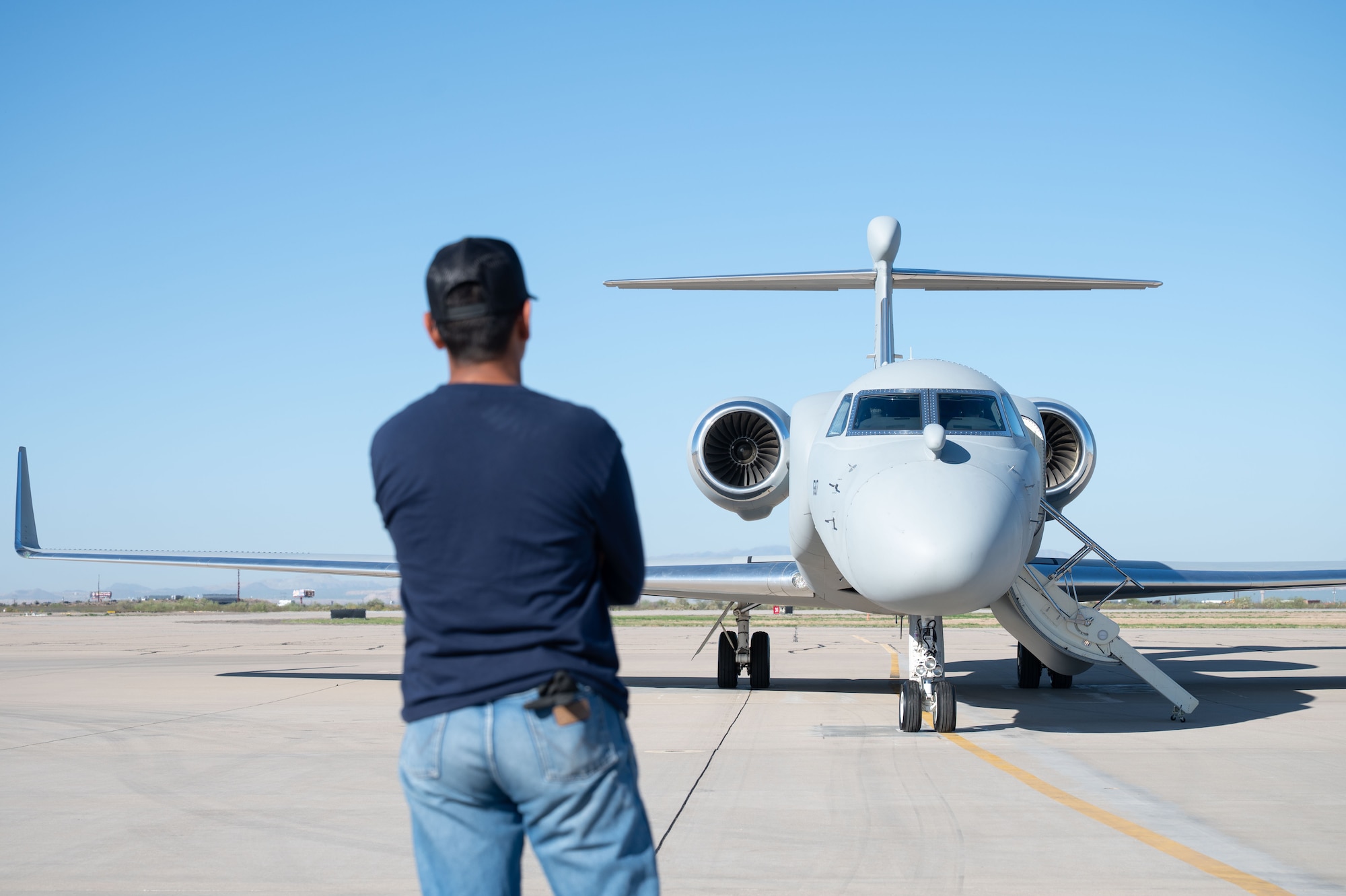 A contracted air marshal guides a U.S. Air Force EA-37B Compass Call aircraft assigned to the 43rd Electronic Combat Squadron at Davis-Monthan Air Force Base, Arizona, July 24, 2025. The EA-37B is designed to disrupt enemy command and control communications, radars and navigation systems. (U.S. Air Force photo by Airman Jaden Kidd)