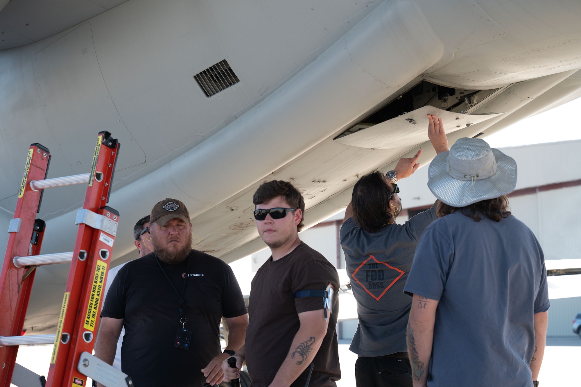 A group of contracted civilian maintainers perform final checks on an EA-37B Compass Call aircraft assigned to the 43rd Electronic Combat Squadron at Davis-Monthan Air Force Base, Arizona, July 24, 2025. All EA-37B maintenance was performed by contractors, while U.S. Air Force pilots handled operations. (U.S. Air Force photo by Airman Jaden Kidd) (This photo was edited to blur a badge using Photoshop.)