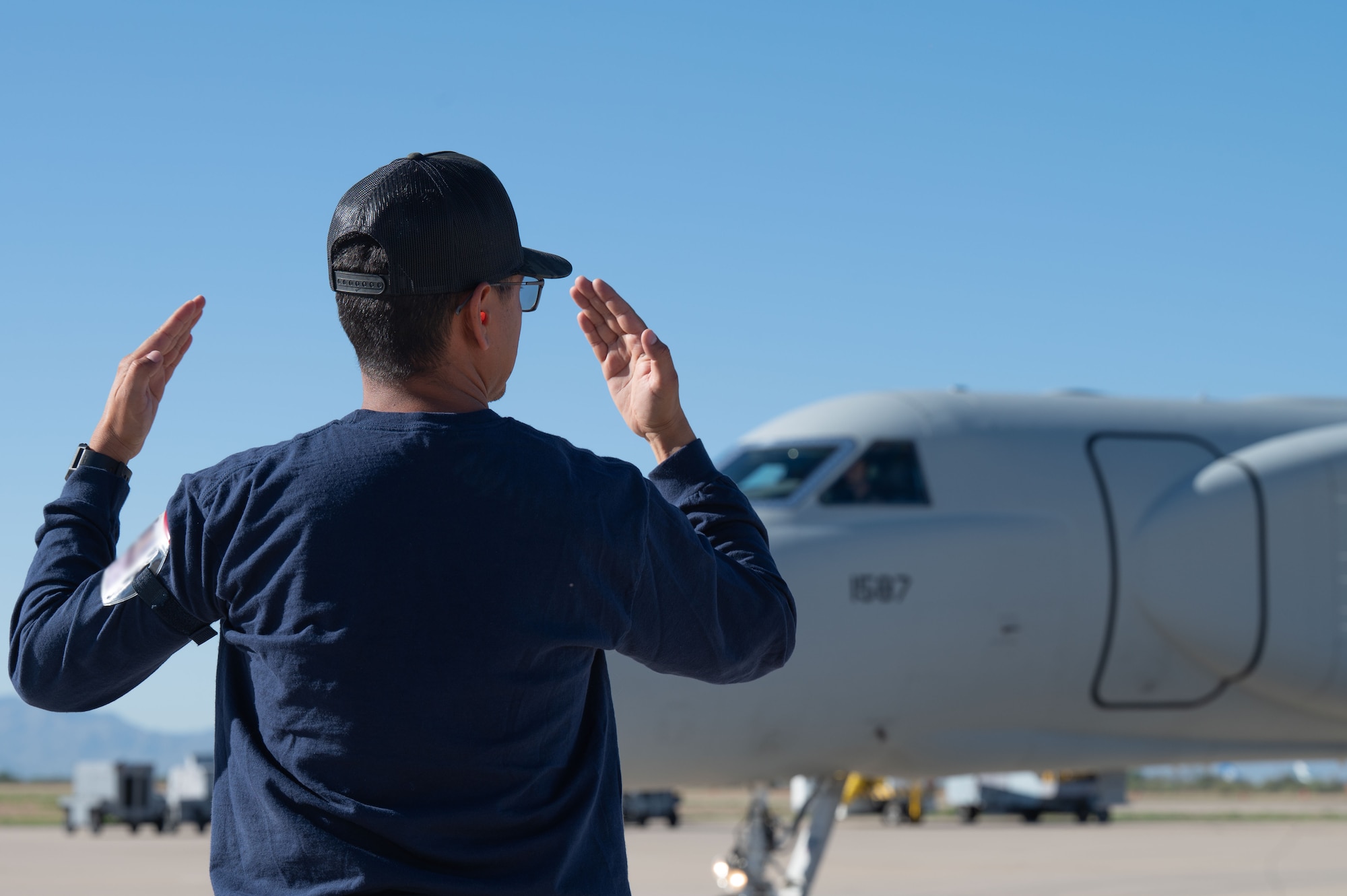 A contracted air marshal guides a U.S. Air Force EA-37B Compass Call aircraft assigned to the 43rd Electronic Combat Squadron as it taxis down the runway at Davis-Monthan Air Force Base, Arizona, July 24, 2025. The EA-37B is designed to significantly hinder adversary coordination as part of the counter-command, control, communications, computers, cyber, intelligence, surveillance and reconnaissance (C5ISR) targeting mission. (U.S. Air Force photo by Airman Jaden Kidd) (This photo was edited to blur a badge using Photoshop.)