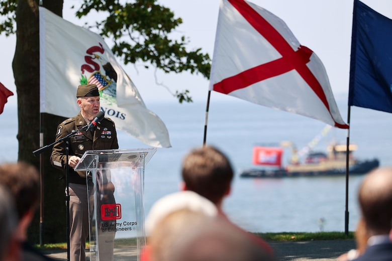 A man in an Army officer uniform speaks outdoors at a podium.