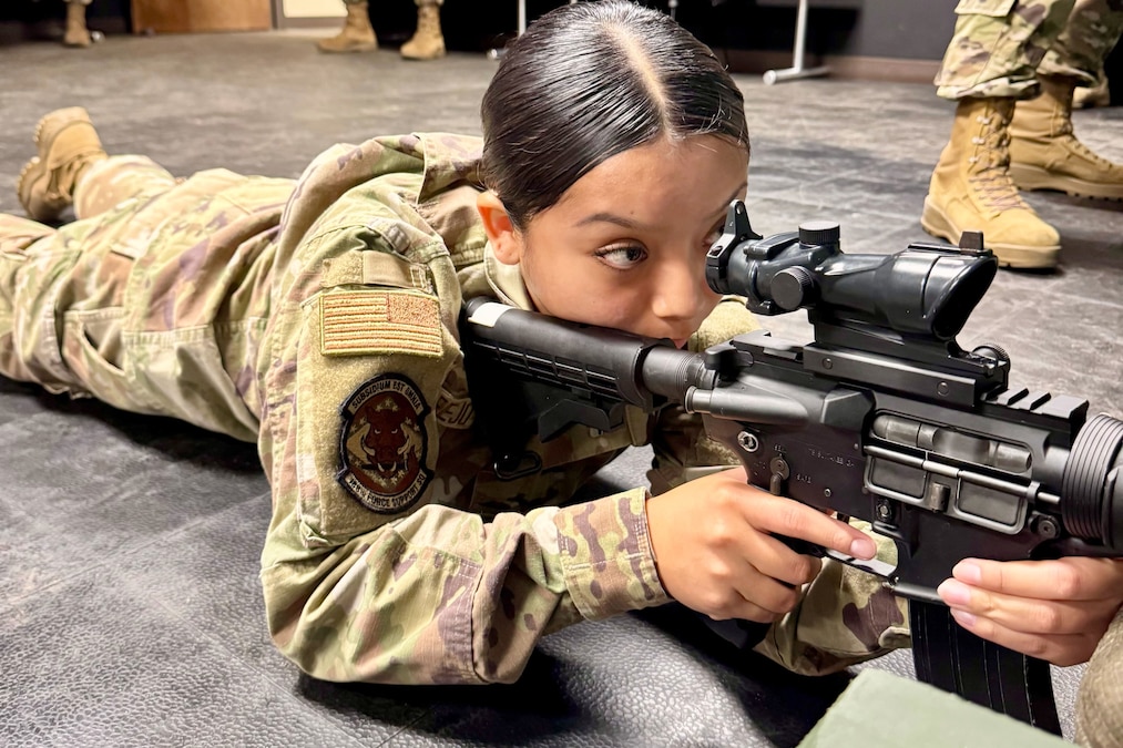 An airman looks through the scope of a weapon while lying on the ground.