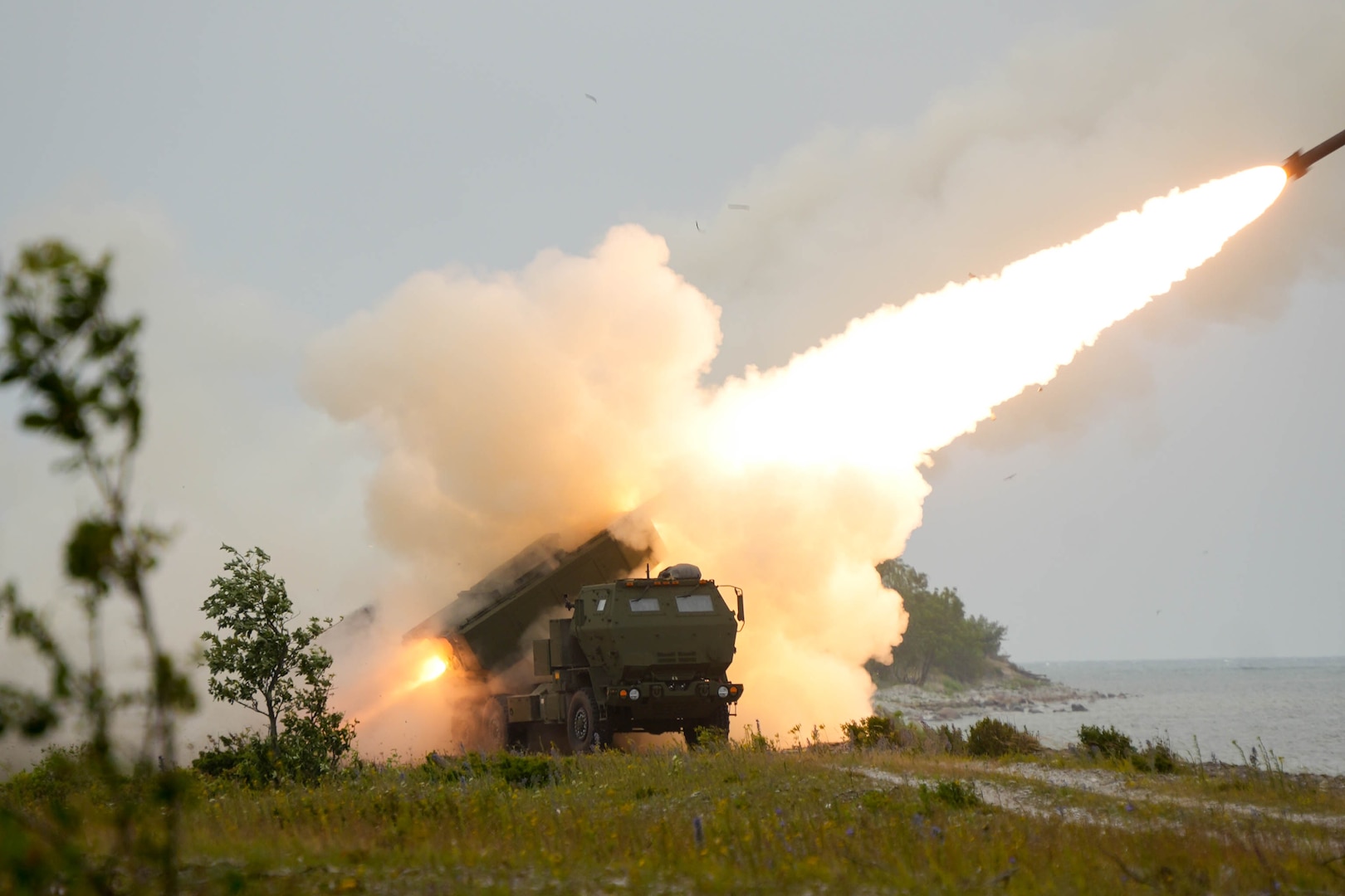 Flames shoot out of a rocket tube mounted on a truck as a missile soars over the ocean.