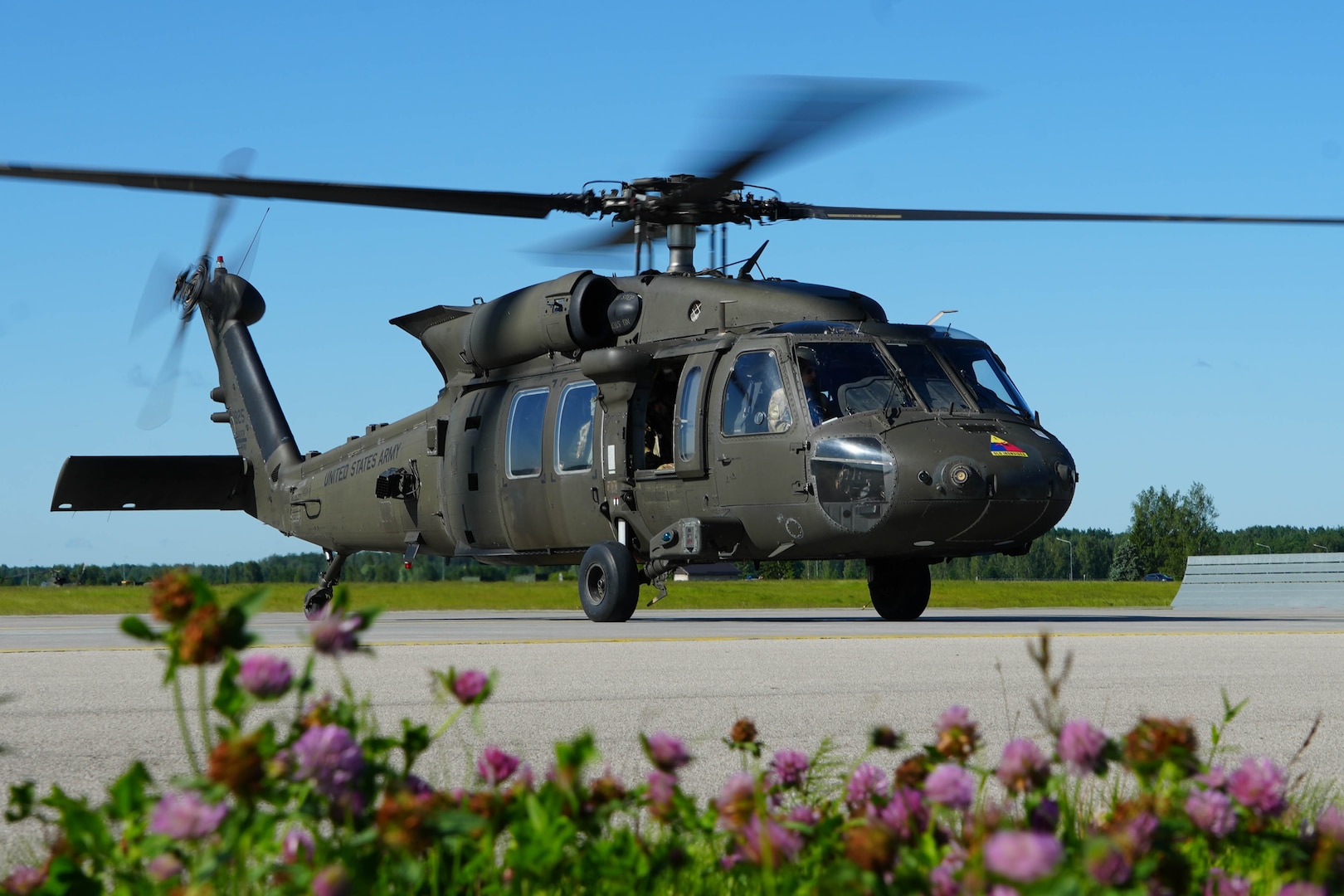Helicopter blades spin as the bird sits on the tarmac with flowers nearby.
