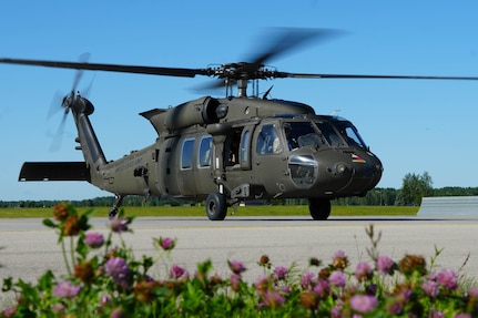 Helicopter blades spin as the bird sits on the tarmac with flowers nearby.