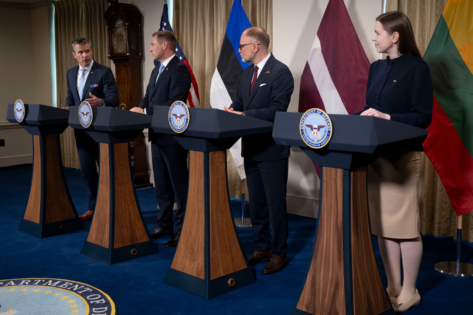 Four people stand at podiums during a briefing.
