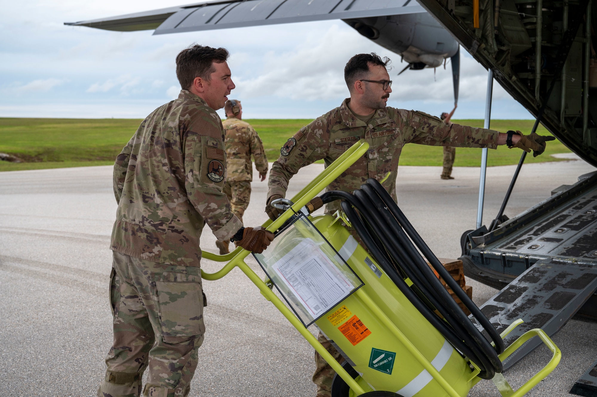 Two Airmen are seen pushing a fire extinguisher out of the cargo bay of a C-130J Hercules. The Airmen to the right is pointing at where he wants the fire extinguisher moved to.