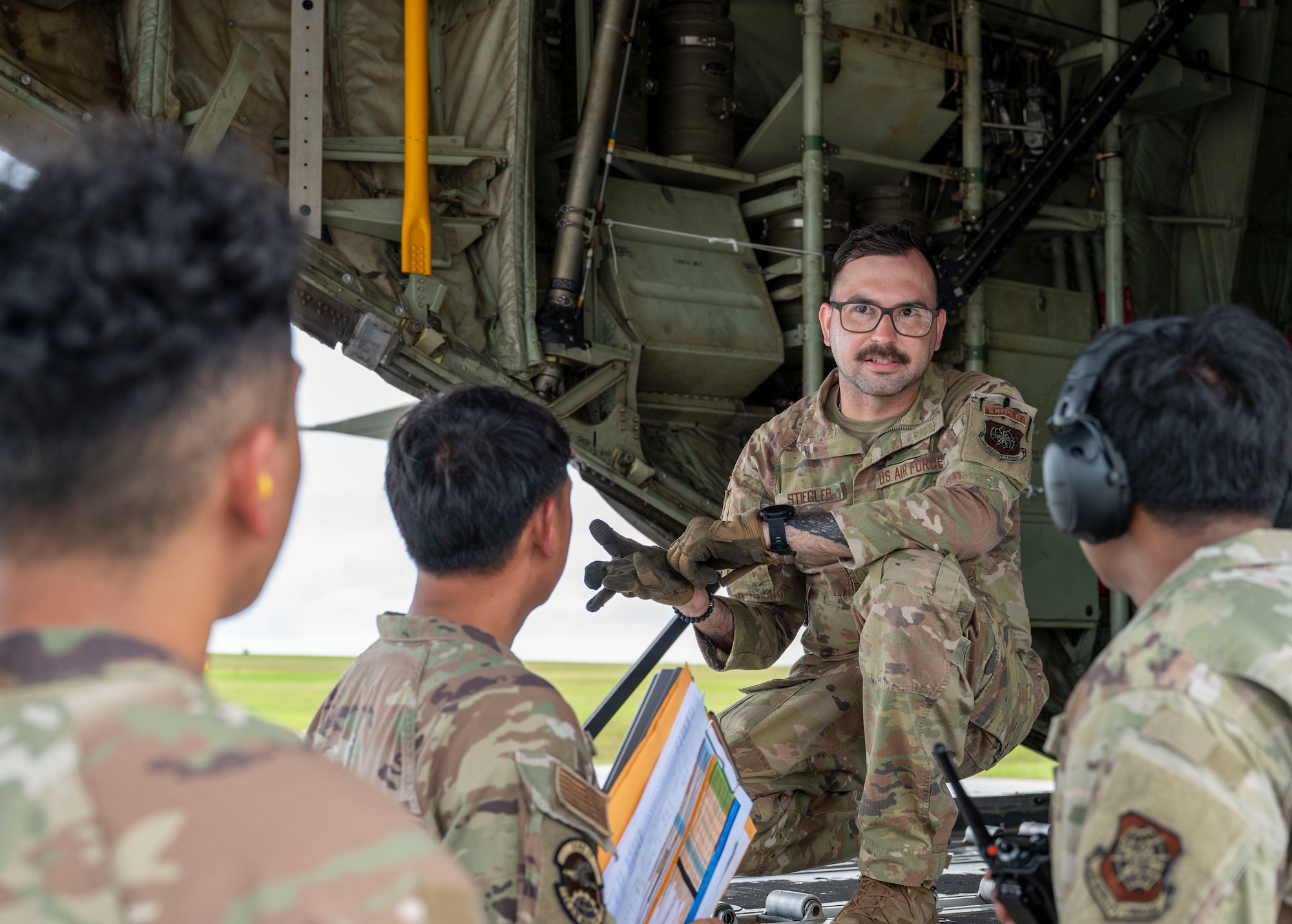 Staff Sgt. James Stiegler briefs Airmen after arriving to Andersen Air Force Base, Guam, at the edge of a cargo bay of a C-130J Hercules.