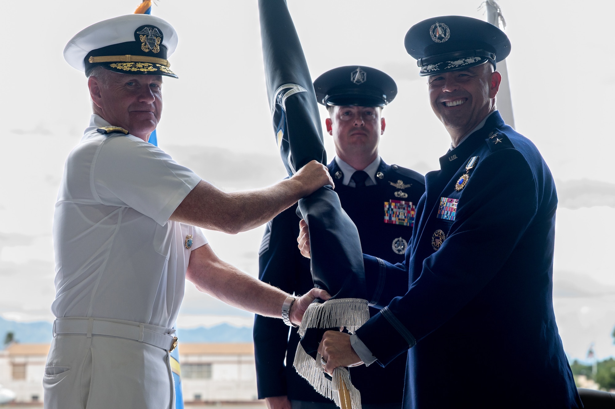 Two men in uniform pass a flag between them