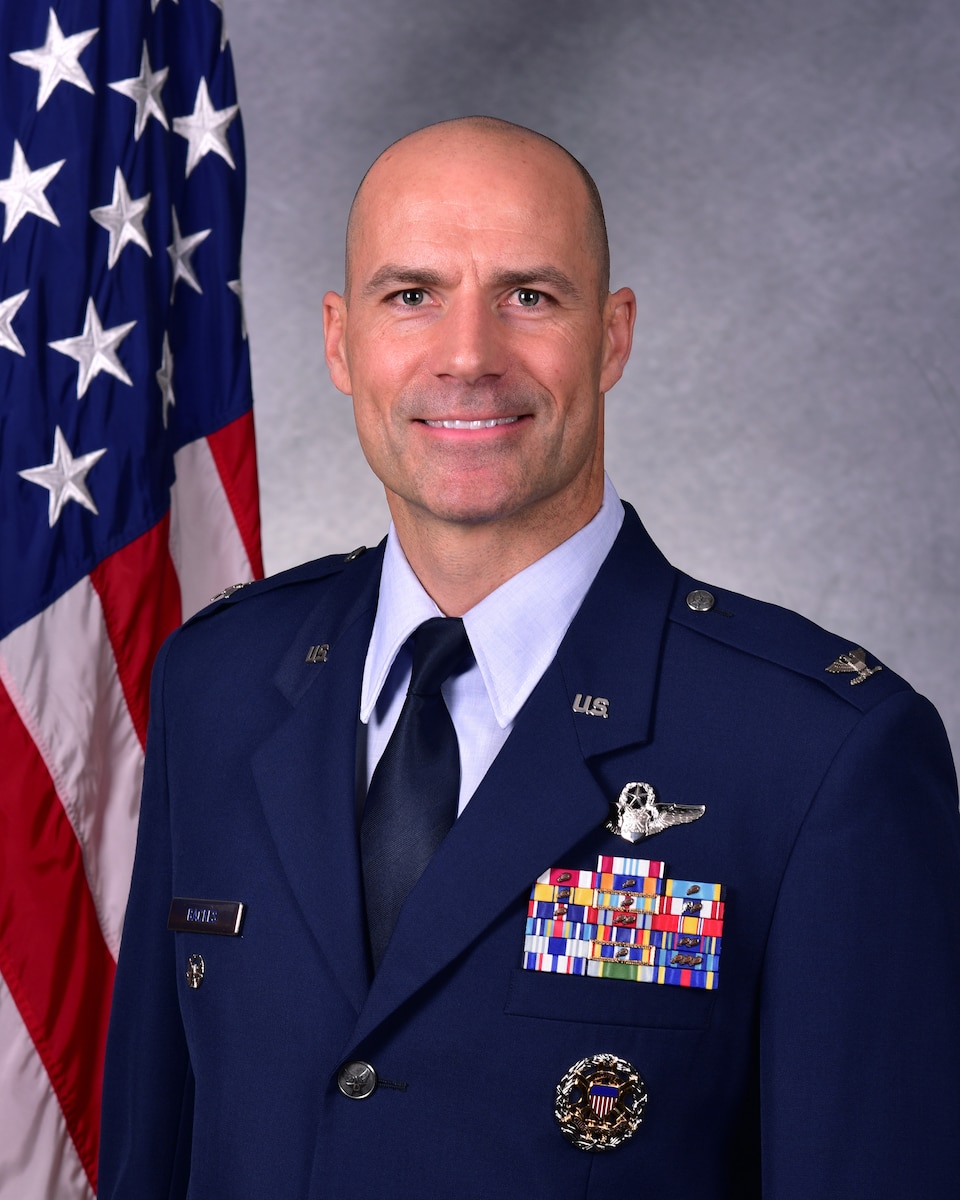 Man in uniform poses for photo in front of flag