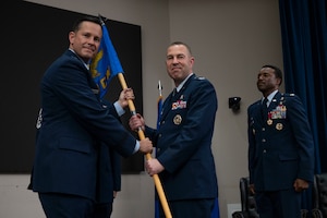 Col. Joshua Garrison assumes command of the 960th Cyberspace Wing and receives the wing guidon from 10th Air Force commander Brig. Gen. Kevin Merrill during the 960th Cyberspace Wing change of command ceremony at JBSA-Lackland, Texas on July 12, 2025. (US Air Force photo by TSgt Melissa Estevez)