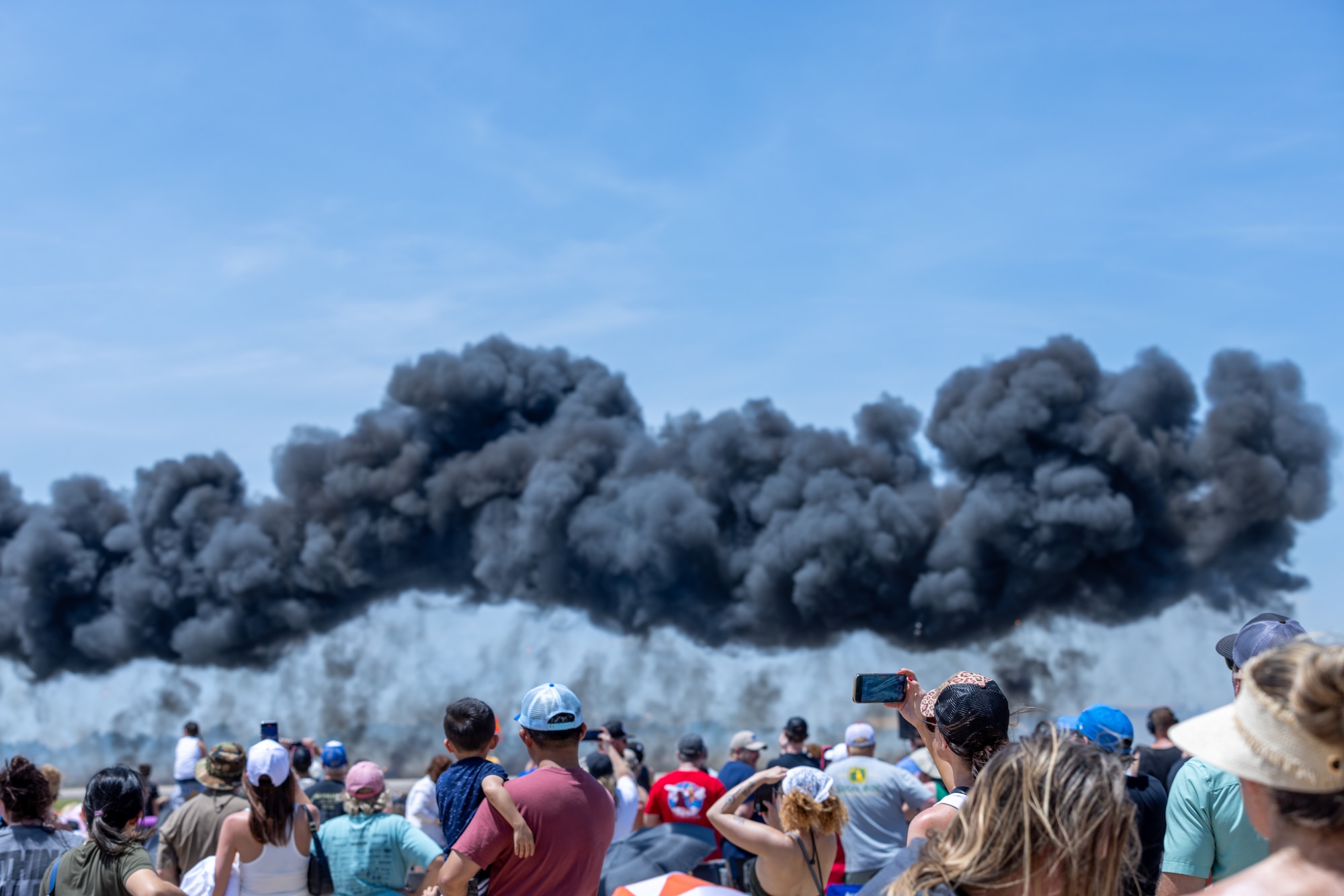 Crowd watching smoke from aircraft at airshow.