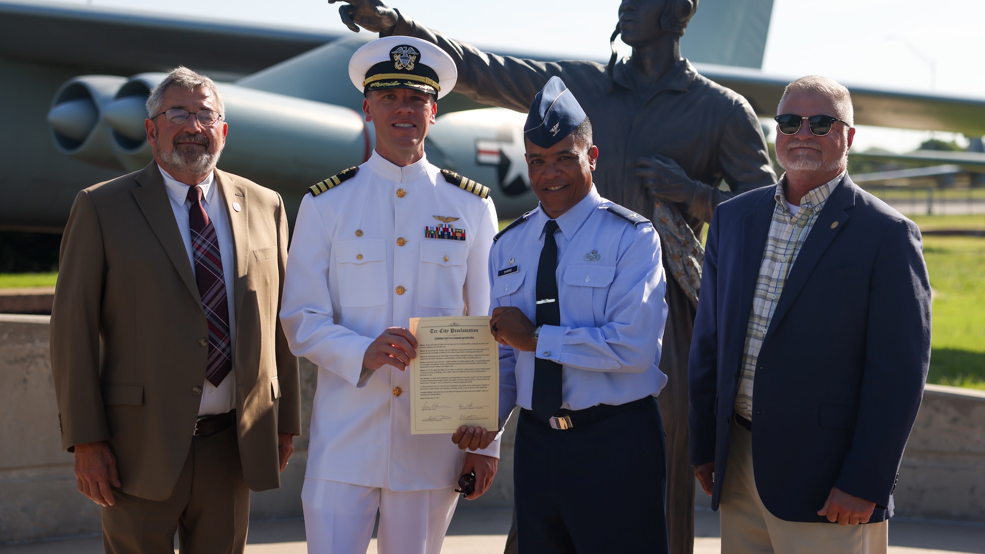 Four men stand in front of plane with document.