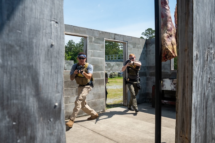 Two men holding fake guns are training to sweep a room