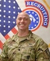 Male Soldier smiles while standing in front of the American flag and the US Army Recruiting Command flag