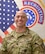 Male Soldier smiles while standing in front of the American flag and the US Army Recruiting Command flag