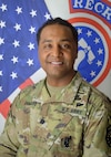 Smiling Army Soldier poses in front of the American and United States Army Recruiting Command flags