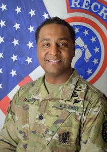 Smiling Army Soldier poses in front of the American and United States Army Recruiting Command flags
