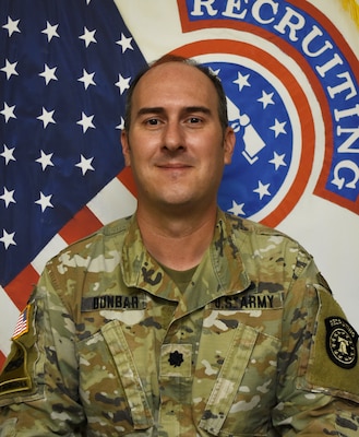 Soldier smiles while posing in front of American flag and United States Army Recruiting Command flag.
