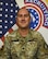 Soldier smiles while posing in front of American flag and United States Army Recruiting Command flag.
