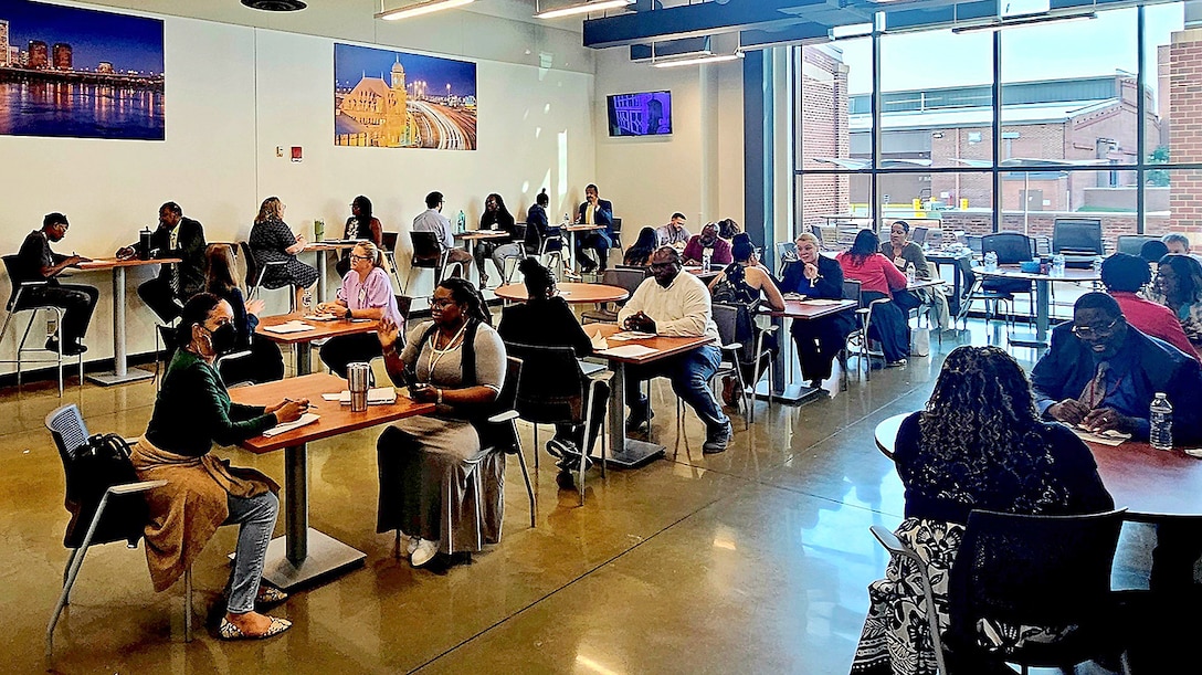 There is a group of tables with people seating on two sides.
