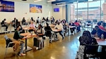 There is a group of tables with people seating on two sides.