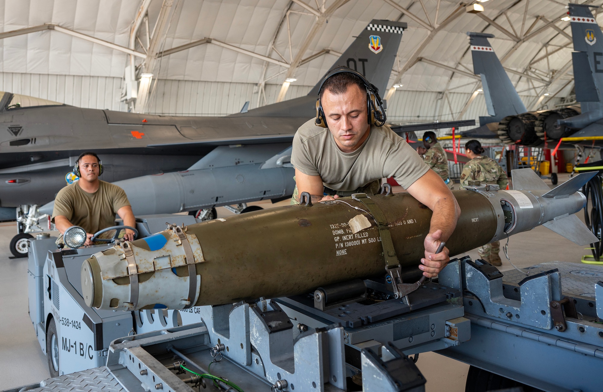 Load crew members strap down a GBU-38 Joint Direct Attack Munition to a jammer driven by another Airman.