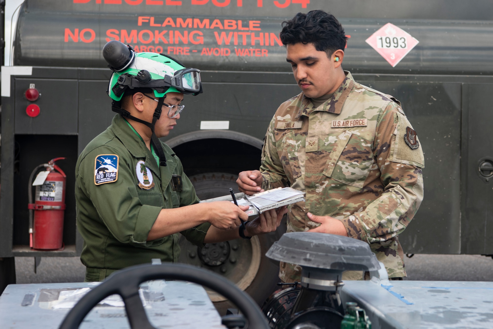U.S. Marine Corps Lance Cpl. Daniel Siaotong, Marine Fighter Attack Squadron 121 avionics mechanic, left, gives documents to U.S. Air Force Senior Airman Amzy Zalvia, 433rd Logistics Readiness Squadron fuels specialist, to complete a refueling operation during Red Flag Alaska 25-3 at Eielson Air Force Base, Alaska, July 25, 2025.