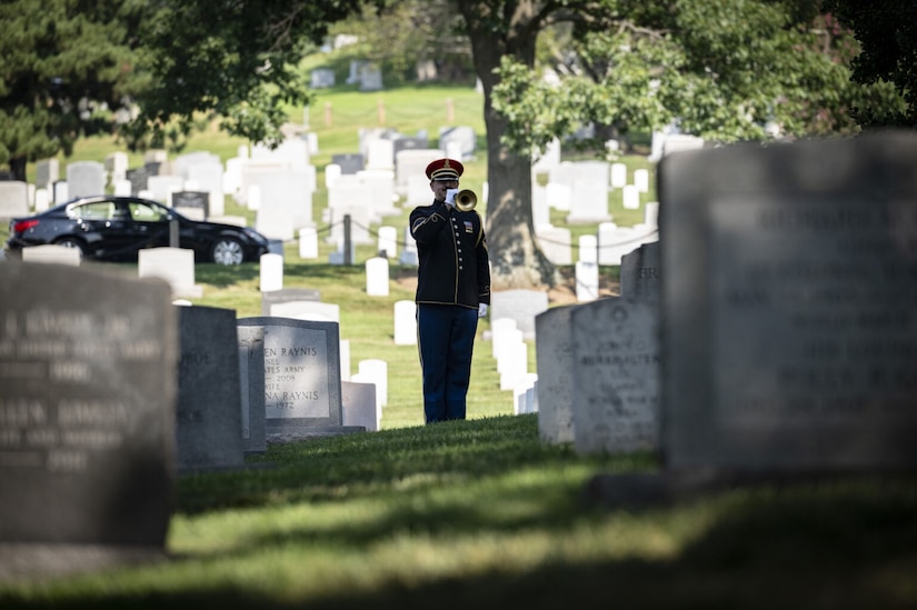 A man dressed in a military uniform plays a bugle in a cemetery.