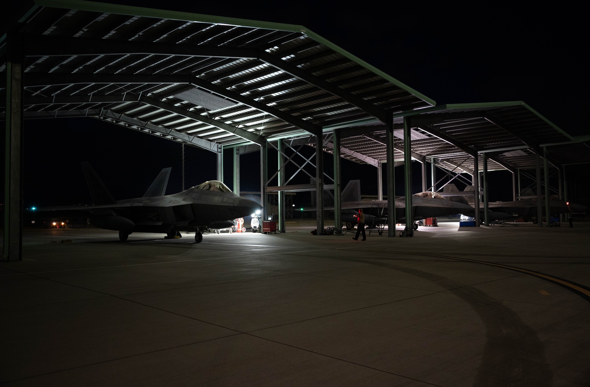 Three F-22 Raptors under hangars at night.