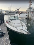 Two Coast Guardsmen are seen standing on a pier next to a white 20-foot center console boat.